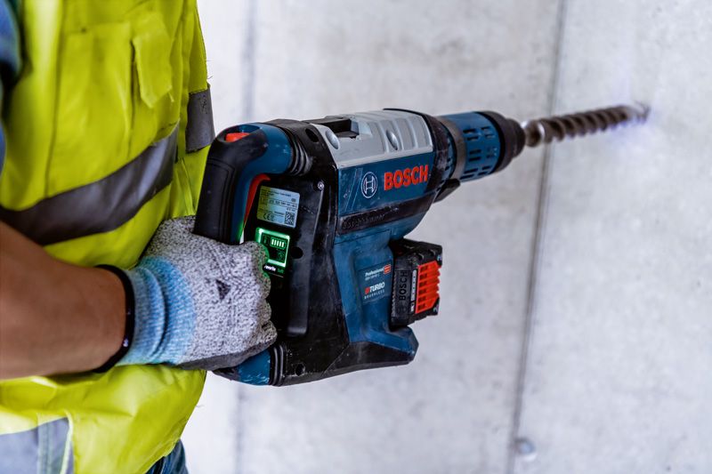 บุคคลที่สวมอุปกรณ์ด้านความปลอดภัยกำลังเจาะเข้าไปในคอนกรีตด้วยค้อนโรตารี่ขนาดใหญ่.