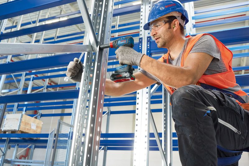 บุคคลที่สวมอุปกรณ์ด้านความปลอดภัยกำลังยึดโครงโลหะโดยใช้สว่านไฟฟ้าไร้สาย.