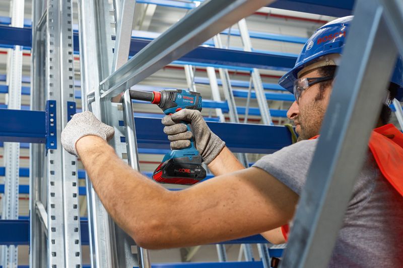 ผู้ที่สวมอุปกรณ์ด้านความปลอดภัยใช้สว่านไร้สายบนโครงโลหะ.