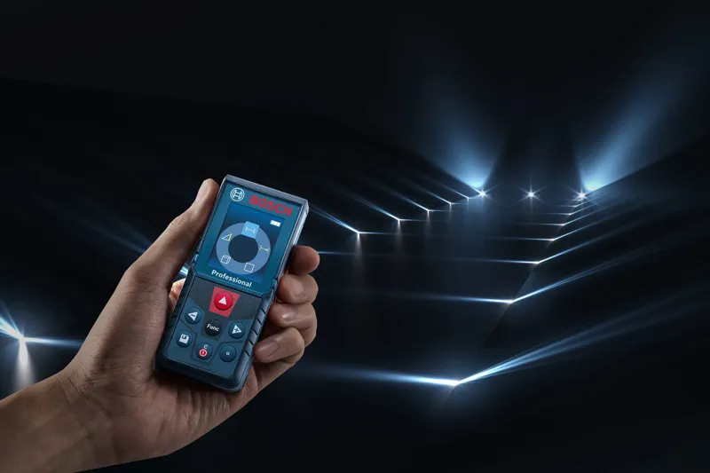 คนๆ หนึ่งกำลังถือเครื่องวัดระยะเลเซอร์ซึ่งฉายลำแสงวัดหลายลำไปทั่วห้องมืด.