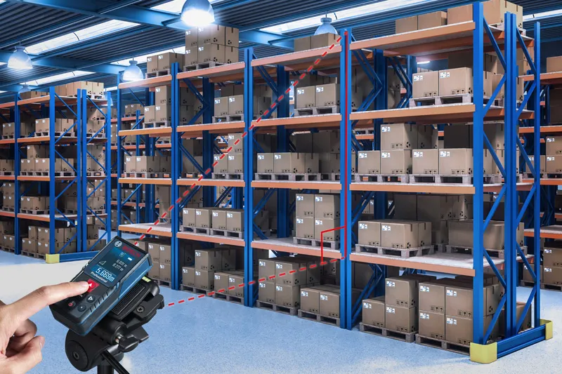 ผู้ใช้เครื่องวัดระยะเลเซอร์เพื่อตรวจสอบระยะห่างระหว่างชั้นวางสินค้าในคลังสินค้า.