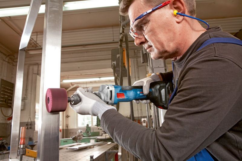 บุคคลที่สวมอุปกรณ์ด้านความปลอดภัยใช้เครื่องเจียรตรงแบบไร้สายบนคานเหล็ก.