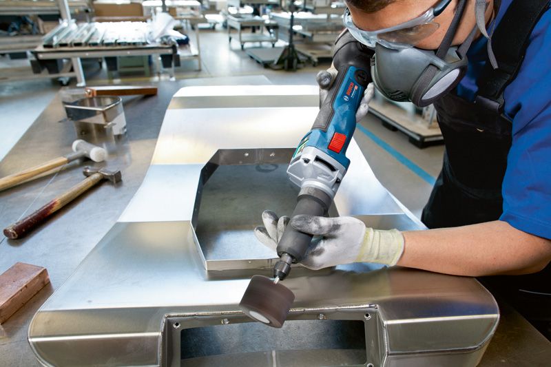 บุคคลที่สวมอุปกรณ์ด้านความปลอดภัยกำลังเจียรแผ่นโลหะด้วยเครื่องเจียรตรงแบบไร้สาย.