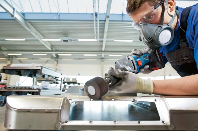 บุคคลที่สวมอุปกรณ์ด้านความปลอดภัยกำลังเจียรพื้นผิวโลหะด้วยเครื่องเจียรตรงแบบไร้สาย.