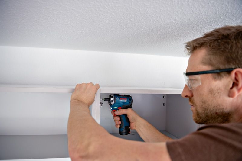 บุคคลที่สวมอุปกรณ์ความปลอดภัยใช้ไขควงไร้สายในการประกอบตู้.