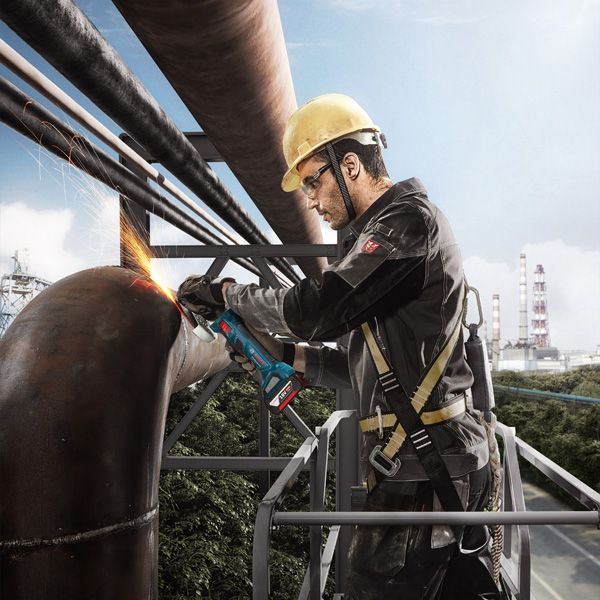 บุคคลที่สวมอุปกรณ์ด้านความปลอดภัยกำลังเจียรท่อโลหะขนาดใหญ่ด้วยเครื่องเจียรแบบมุม.