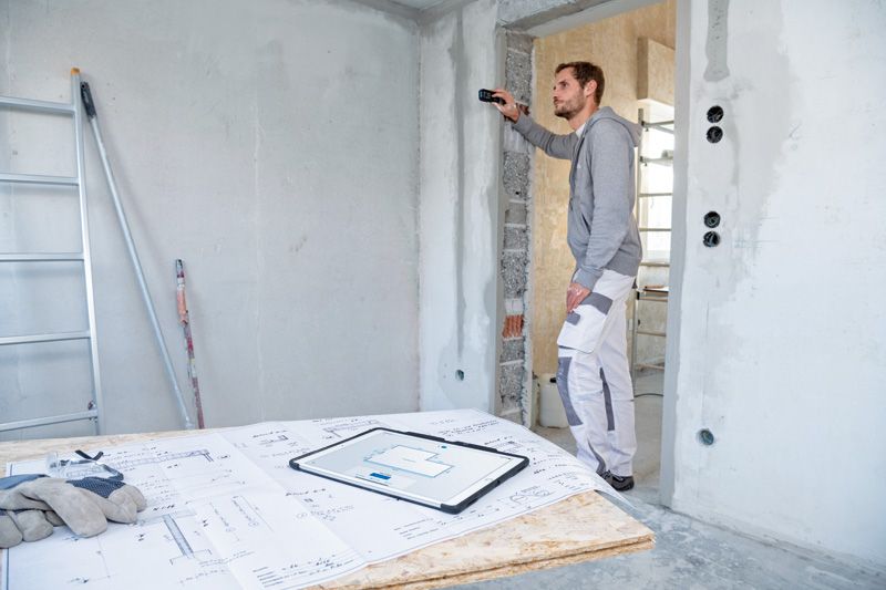 ผู้ใช้เครื่องวัดระยะเลเซอร์ตรวจสอบระยะกำแพงที่ไซต์ก่อสร้าง.