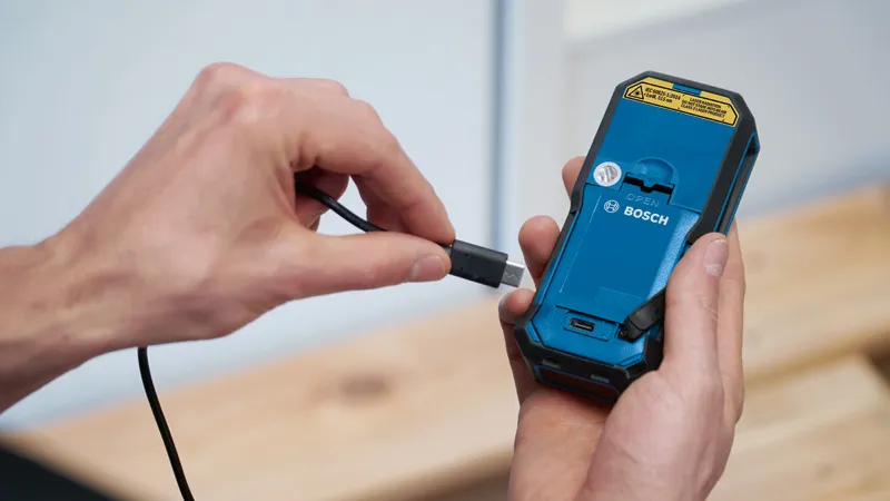 คนๆ หนึ่งกำลังต่อสายชาร์จเข้ากับด้านหลังของเครื่องมือไฟฟ้าแบบพกพา.