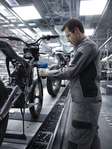 ผู้ที่สวมอุปกรณ์ด้านความปลอดภัยใช้เครื่องมือไฟฟ้าในการประกอบโครงรถจักรยานยนต์.