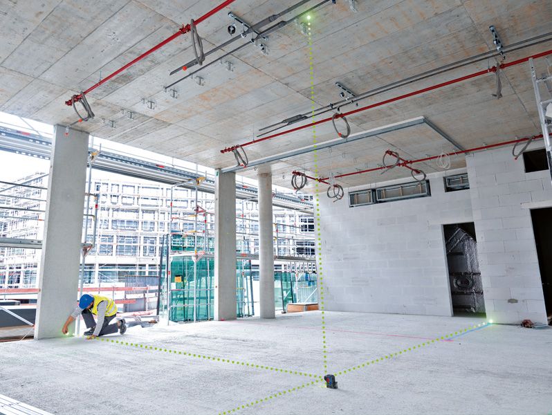 บุคคลที่สวมอุปกรณ์ด้านความปลอดภัยใช้เครื่องมือปรับระดับด้วยเลเซอร์เพื่อจัดตำแหน่งจุดต่างๆ ในพื้นที่ก่อสร้าง