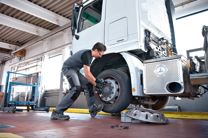 บุคคลที่สวมอุปกรณ์ด้านความปลอดภัยใช้ประแจกระแทกเพื่อขันสลักเกลียวบนล้อรถบรรทุก.