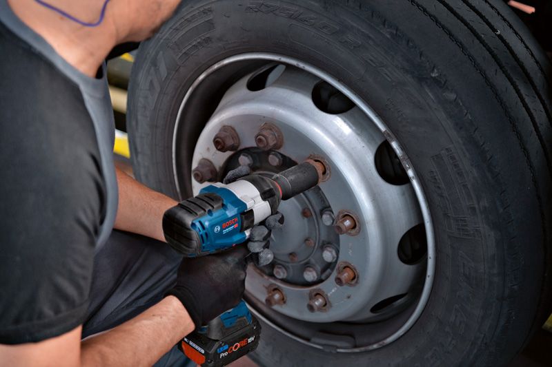 บุคคลที่สวมอุปกรณ์ด้านความปลอดภัยใช้ประแจกระแทกเพื่อขันสลักเกลียวบนล้อรถบรรทุก.