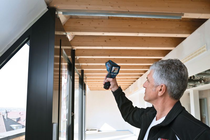 บุคคลหนึ่งใช้เครื่องวัดอุณหภูมิเพื่อตรวจสอบอุณหภูมิบริเวณใกล้คานไม้บนเพดาน