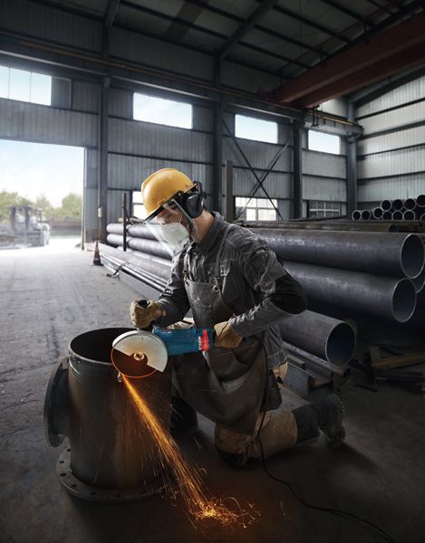 บุคคลที่สวมอุปกรณ์ด้านความปลอดภัยใช้เครื่องเจียรตัดท่อโลหะขนาดใหญ่ในอาคาร.