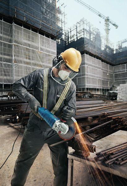 บุคคลที่สวมอุปกรณ์ด้านความปลอดภัยกำลังบดแท่งโลหะด้วยเครื่องเจียรที่ไซต์ก่อสร้าง.
