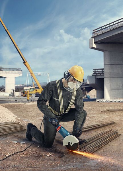 บุคคลที่สวมอุปกรณ์ด้านความปลอดภัยใช้เครื่องเจียรตัดแท่งโลหะในสถานที่ก่อสร้าง.