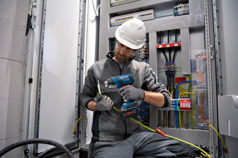 ผู้ที่สวมอุปกรณ์ด้านความปลอดภัยใช้ปืนเป่าลมร้อนแบบไร้สายกับสายไฟ.