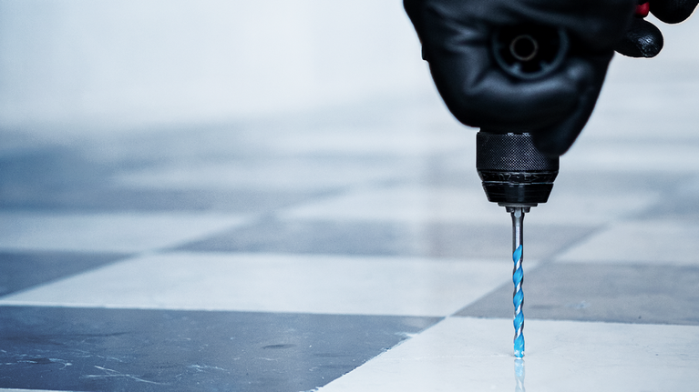 บุคคลที่สวมอุปกรณ์ความปลอดภัยกำลังเจาะลงไปในพื้นกระเบื้อง