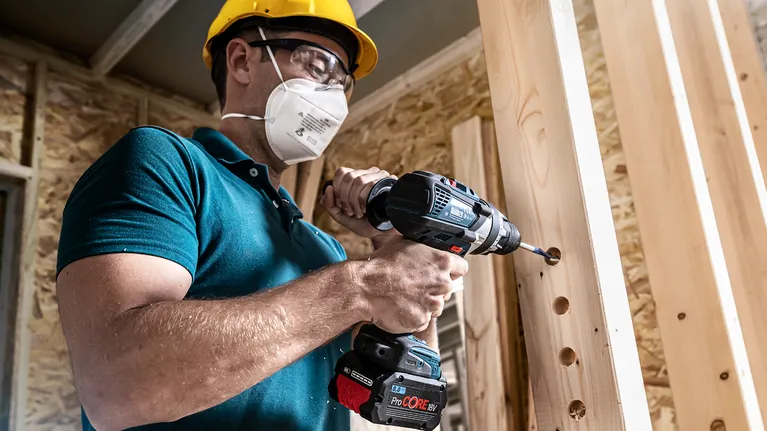 บุคคลที่สวมอุปกรณ์ความปลอดภัยกำลังเจาะรูบนคานไม้