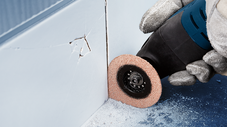 บุคคลที่สวมอุปกรณ์ด้านความปลอดภัยใช้เครื่องมือหมุนเพื่อเจียรบริเวณมุมผนัง