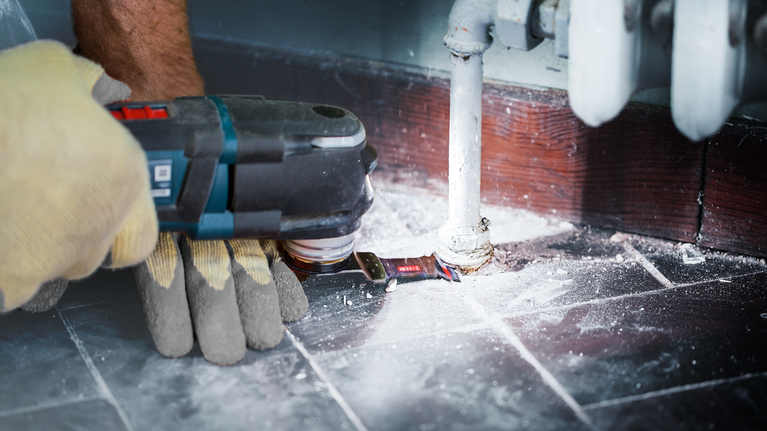 บุคคลที่สวมอุปกรณ์ด้านความปลอดภัยใช้เครื่องมือไฟฟ้าตัดพื้นรอบท่อ