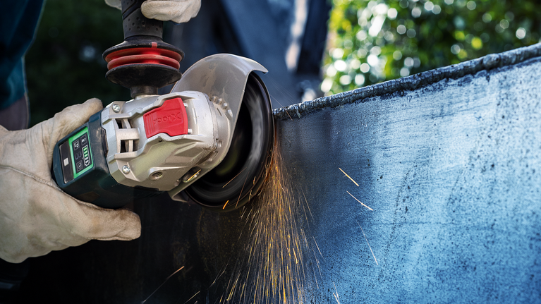 บุคคลที่สวมอุปกรณ์ป้องกันความปลอดภัยกำลังขัดพื้นผิวโลหะด้วยเครื่องเจียรไฟฟ้า