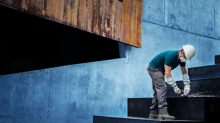 บุคคลที่สวมอุปกรณ์ความปลอดภัยกำลังเจาะบันไดโลหะ