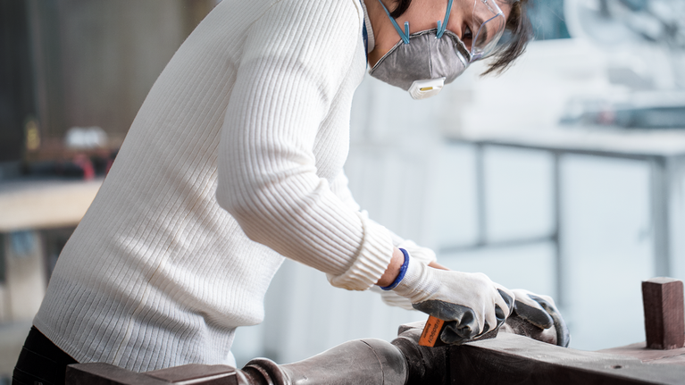 บุคคลที่สวมอุปกรณ์ป้องกันความปลอดภัยกำลังขัดพื้นผิวไม้ด้วยเครื่องมือขัดมือ