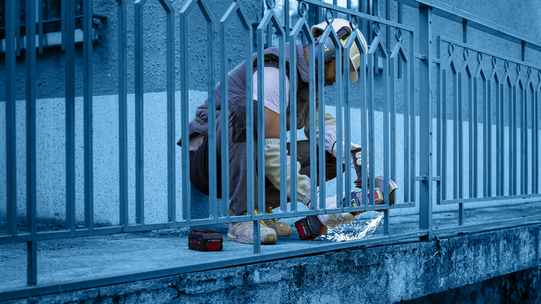 บุคคลที่สวมอุปกรณ์ความปลอดภัยใช้เครื่องมือไฟฟ้าตัดรั้วโลหะ