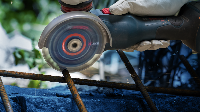 บุคคลที่สวมอุปกรณ์ความปลอดภัยใช้เครื่องเจียรตัดผ่านเหล็กเส้นที่เป็นสนิม