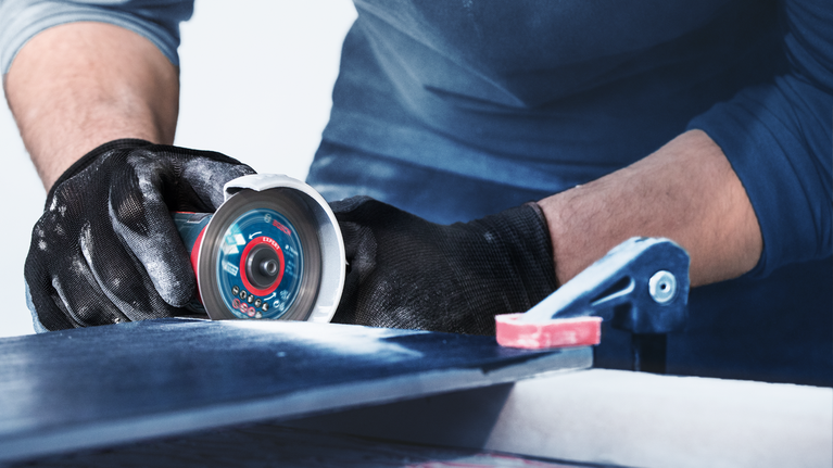 บุคคลที่สวมอุปกรณ์ความปลอดภัยกำลังตัดกระเบื้องด้วยเครื่องมือไฟฟ้า