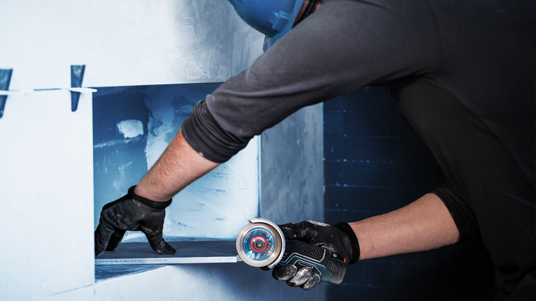 บุคคลที่สวมอุปกรณ์ด้านความปลอดภัยกำลังตัดช่องผนังด้วยเครื่องมือไฟฟ้าขนาดกะทัดรัด