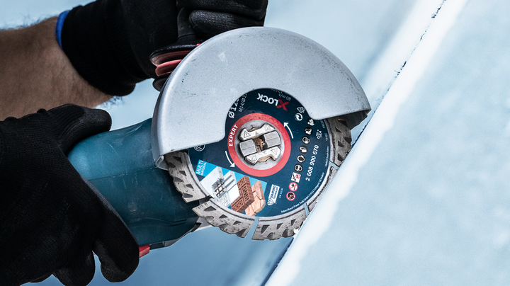 บุคคลที่สวมอุปกรณ์ความปลอดภัยกำลังตัดกระเบื้องโดยใช้เครื่องเจียร