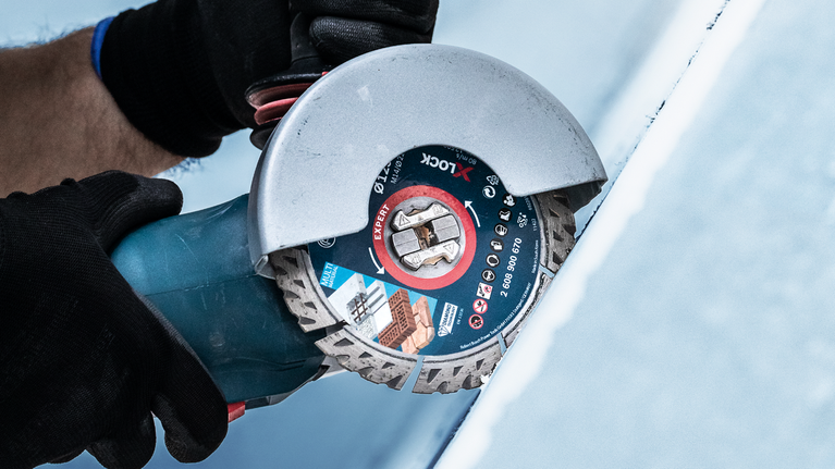 บุคคลที่สวมอุปกรณ์ความปลอดภัยกำลังตัดกระเบื้องโดยใช้เครื่องเจียร