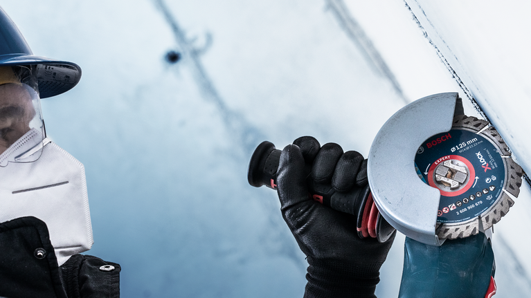 บุคคลที่สวมอุปกรณ์ด้านความปลอดภัยใช้เครื่องเจียรตัดพื้นผิวโลหะ