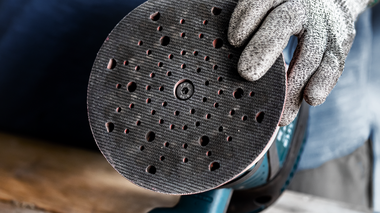 บุคคลที่สวมอุปกรณ์ด้านความปลอดภัยถือเครื่องขัดแบบวงกลมที่มีแผ่นขัดแบบมีรูพรุน