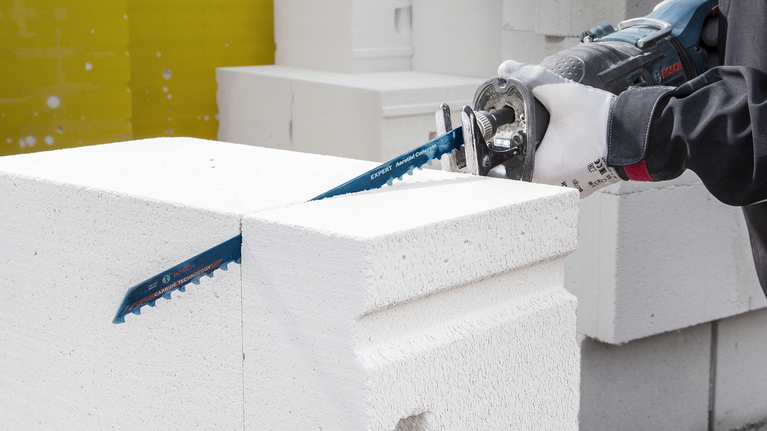 บุคคลที่สวมอุปกรณ์ความปลอดภัยกำลังตัดบล็อกคอนกรีตสีขาวด้วยเลื่อยตัดโลหะ