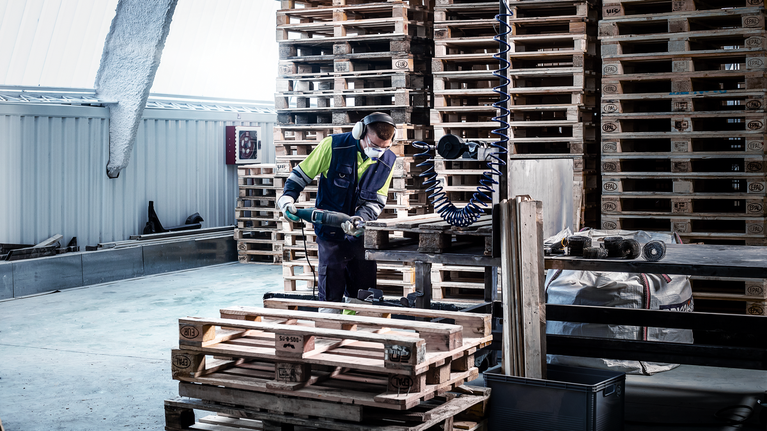 บุคคลที่สวมอุปกรณ์ด้านความปลอดภัยใช้เครื่องมือไฟฟ้าตัดพาเลทไม้