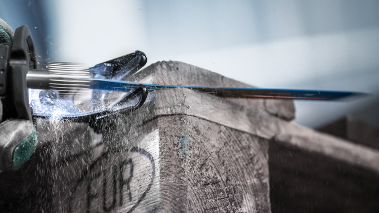 บุคคลที่สวมอุปกรณ์ความปลอดภัยใช้เลื่อยตัดโลหะตัดผ่านลังไม้