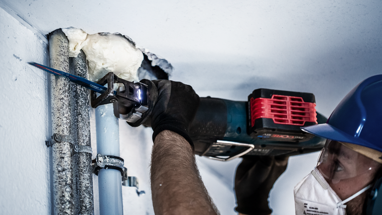 บุคคลที่สวมอุปกรณ์ด้านความปลอดภัยกำลังตัดผ่านท่อโลหะโดยใช้เลื่อยตัดโลหะแบบลูกสูบ