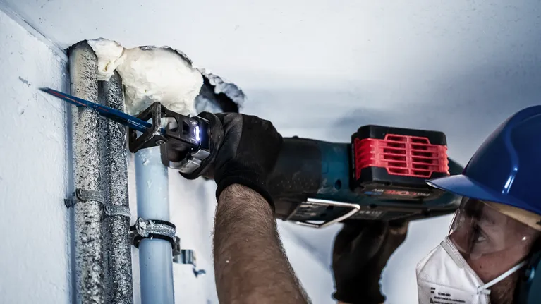 บุคคลที่สวมอุปกรณ์ด้านความปลอดภัยกำลังตัดผ่านท่อโลหะโดยใช้เลื่อยตัดโลหะแบบลูกสูบ