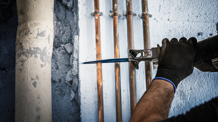 คนกำลังใช้เลื่อยตัดท่อทองแดงที่ติดตั้งบนผนัง