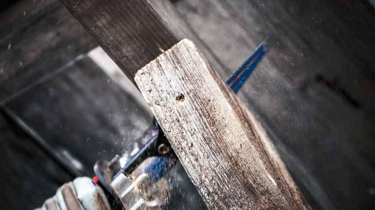 บุคคลที่สวมอุปกรณ์ความปลอดภัยกำลังตัดไม้กระดานด้วยเลื่อยตัดโลหะ