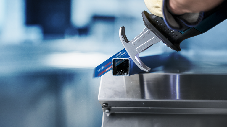 บุคคลที่สวมอุปกรณ์ด้านความปลอดภัยใช้เลื่อยตัดท่อโลหะ