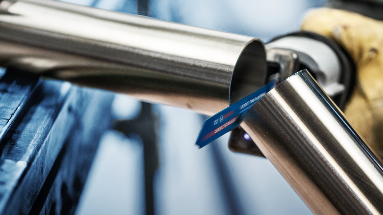 บุคคลที่สวมอุปกรณ์ความปลอดภัยกำลังตัดท่อโลหะด้วยเลื่อยตัดโลหะแบบลูกสูบ