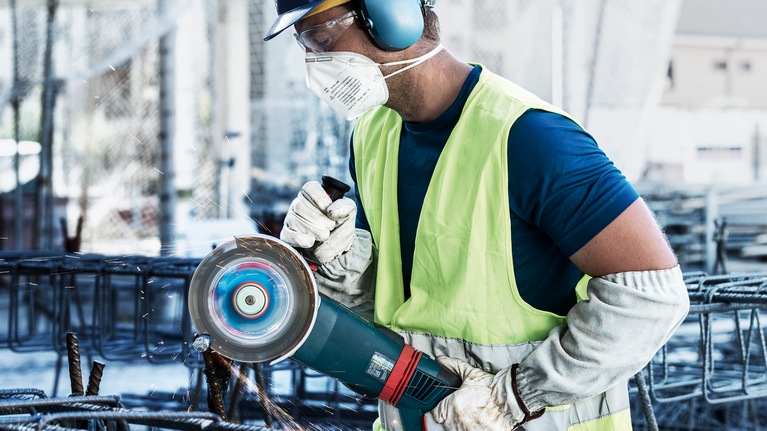 บุคคลที่สวมอุปกรณ์ความปลอดภัยกำลังตัดเหล็กเส้นด้วยเลื่อยวงกลม ทำให้เกิดประกายไฟ