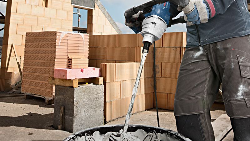 บุคคลที่สวมอุปกรณ์ความปลอดภัยกำลังใช้งานเครื่องผสมเพื่อผสมปูนซีเมนต์