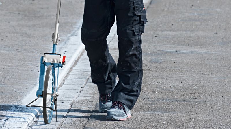 บุคคลที่สวมอุปกรณ์ความปลอดภัยจะวัดระยะทางบนถนนด้วยล้อวัด