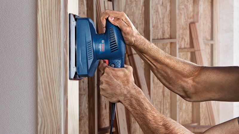 คนกำลังขัดพื้นไม้ด้วยเครื่องขัดกระดาษทรายแบบวงโคจร