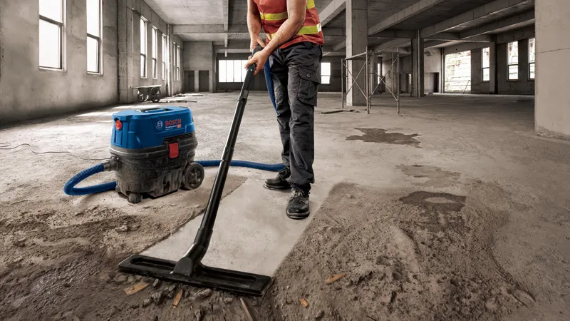 บุคคลที่สวมอุปกรณ์ด้านความปลอดภัยกำลังดูดฝุ่นคอนกรีตในอาคารขนาดใหญ่ที่ยังสร้างไม่เสร็จ.